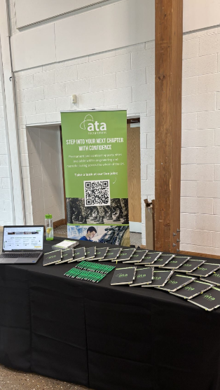 Two people standing in front of an ATA Recruitment Forces banner at a recruitment event, engaging with visitors about career opportunities for ex forces professionals.